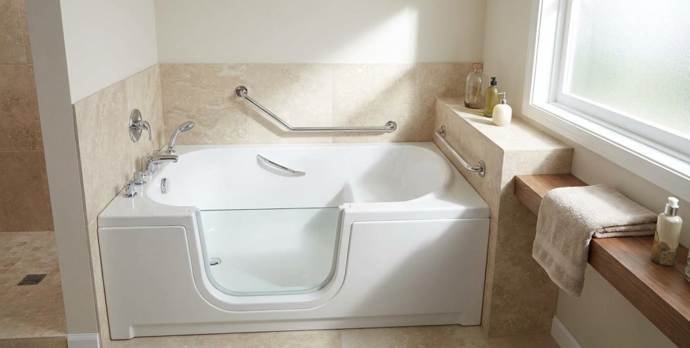 Walk-in bathtub with glass door and grab bars in a bright tiled bathroom with window shelf